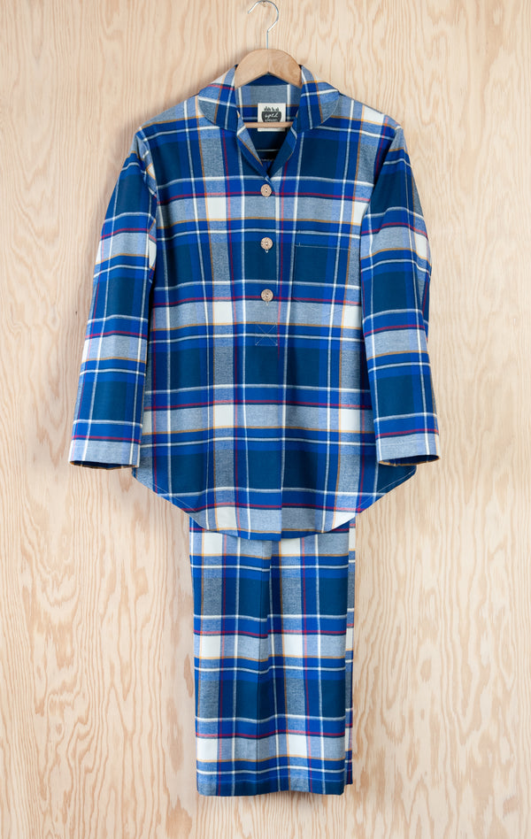 Women's Emilia Pajama set in vibrant blue and white plaid with a narrow red band component..  Pop-over style tunic top with three buttons, long sleeves, and a peter pan collar.  Pajama Pants are full length with an elastic waistband and inseam pockets.